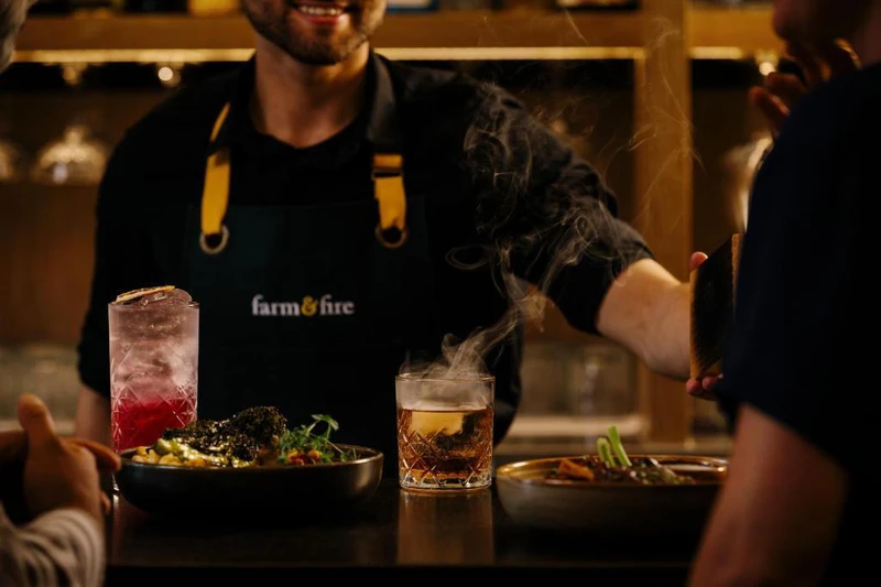 Person serving a couple cocktails and plates of food at the bar