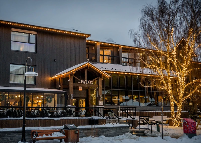 A snowy restaurant exterior in the fading light, illuminated by its windows and fairylights