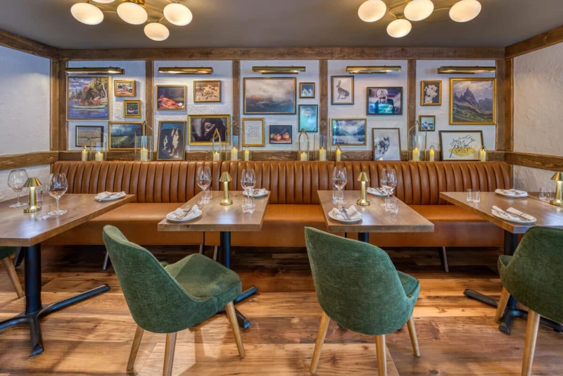 Fat Ox Restaurant interior showing empty tables, leather benches and green upholstered chairs.