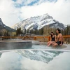 Couple sit in outdoor hot pool with a snowy mountain backdrop