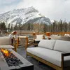 Firepit burns in front of cushioned outdoor seating with a mountain backdrop