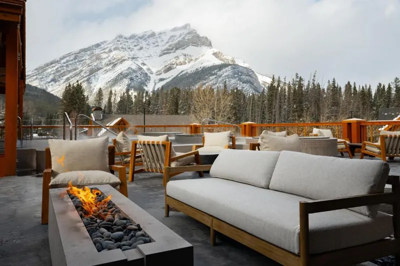 Firepit burns in front of cushioned outdoor seating with a mountain backdrop